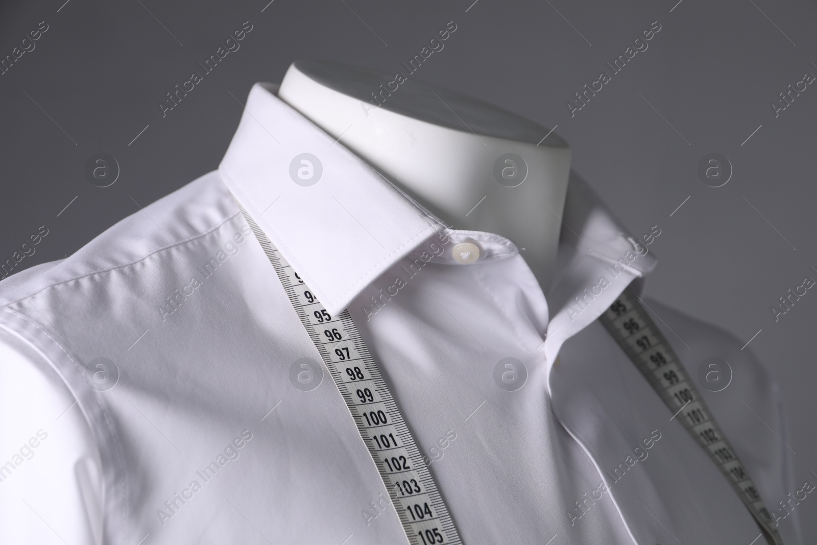 Photo of Male mannequin with white shirt and measuring tape on grey background, closeup