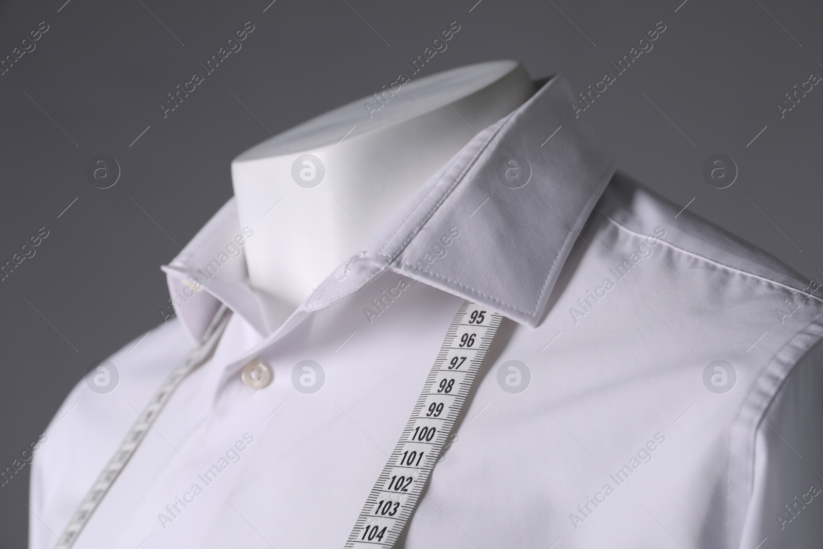 Photo of Male mannequin with white shirt and measuring tape on grey background, closeup