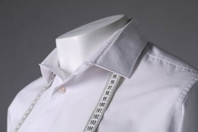 Male mannequin with white shirt and measuring tape on grey background, closeup