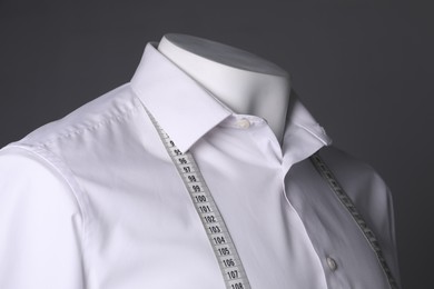 Male mannequin with white shirt and measuring tape on grey background, closeup