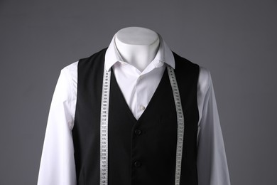 Male mannequin with black vest, white shirt and measuring tape on grey background