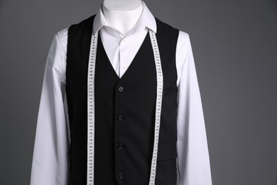 Male mannequin with black vest, white shirt and measuring tape on grey background