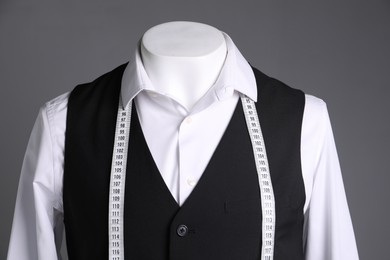 Male mannequin with black vest, white shirt and measuring tape on grey background, closeup