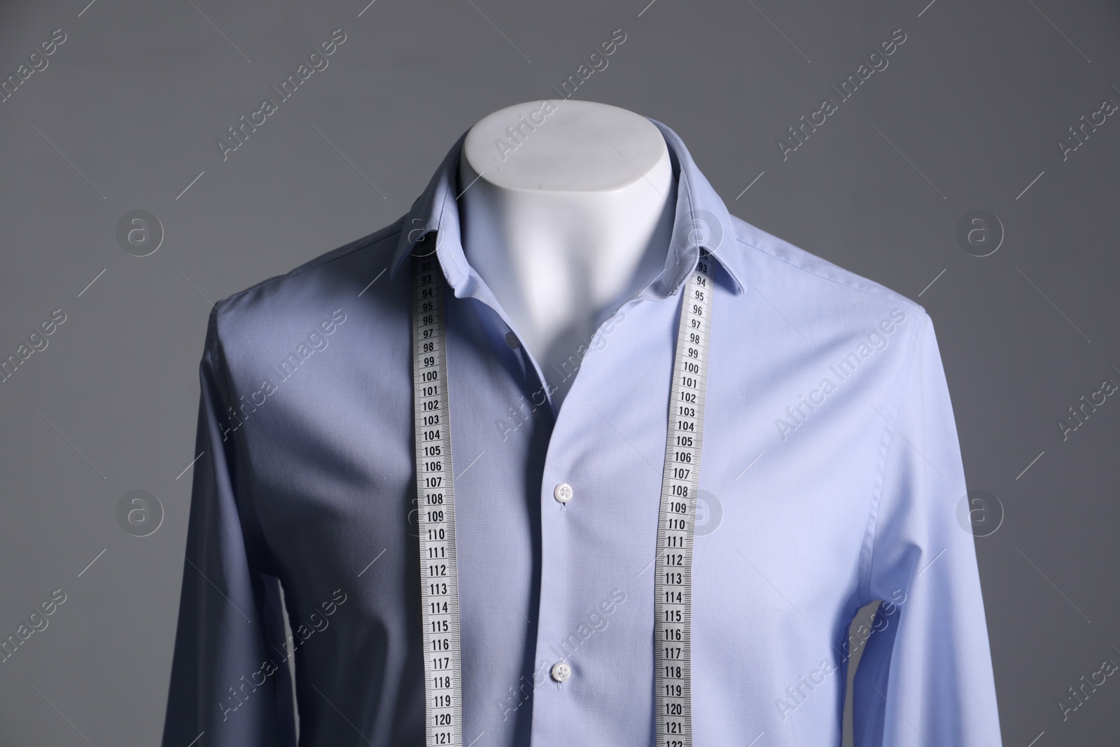 Photo of Male mannequin with light blue shirt and measuring tape on grey background