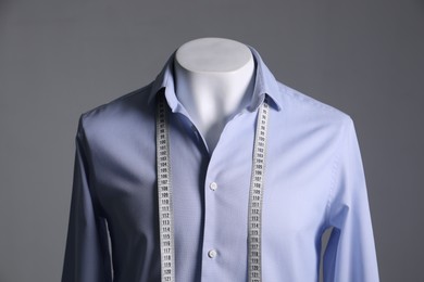 Male mannequin with light blue shirt and measuring tape on grey background