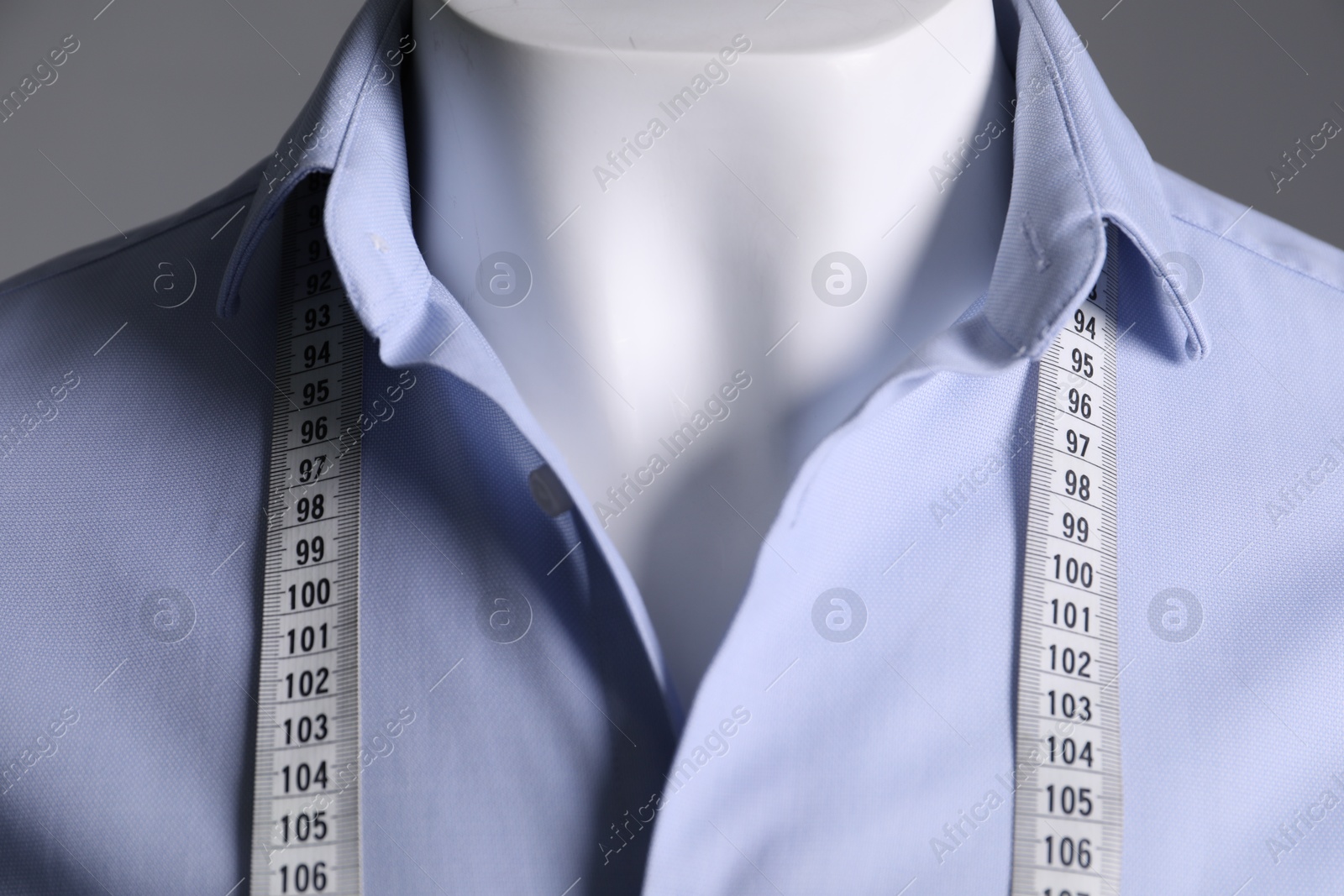 Photo of Male mannequin with light blue shirt and measuring tape on grey background, closeup