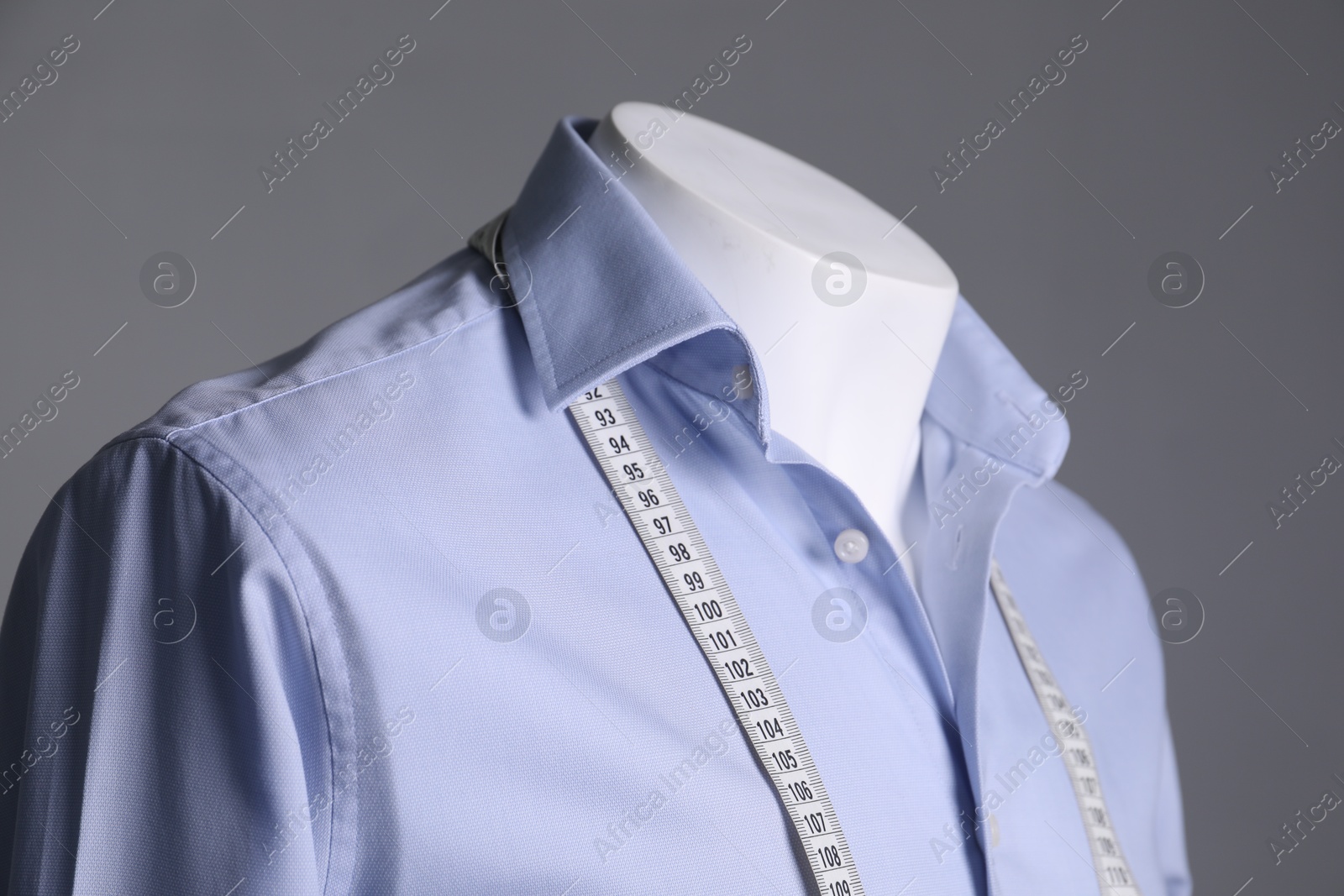 Photo of Male mannequin with light blue shirt and measuring tape on grey background, closeup