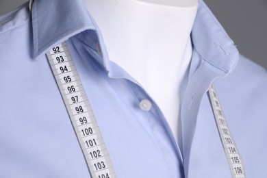 Male mannequin with light blue shirt and measuring tape on grey background, closeup