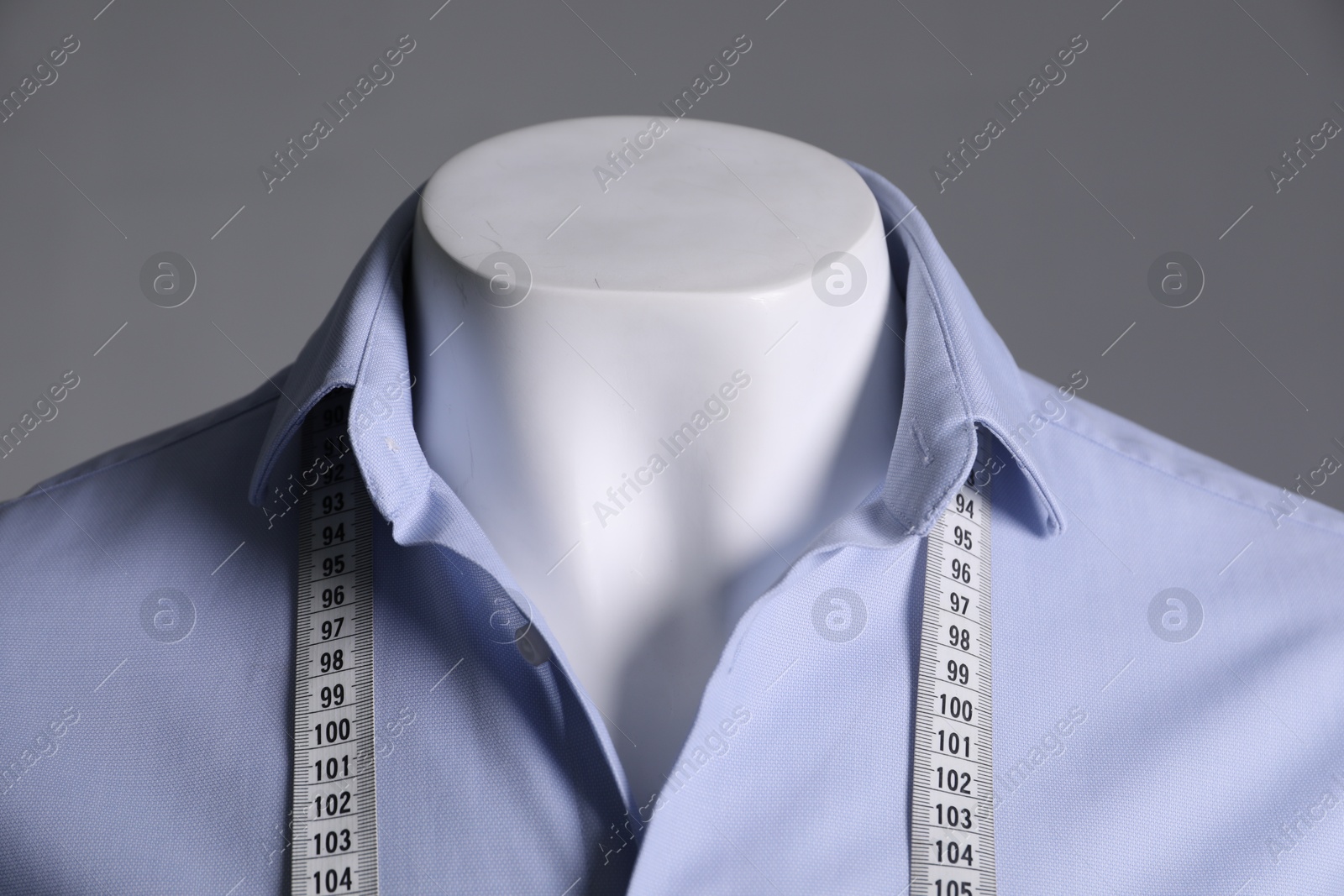 Photo of Male mannequin with light blue shirt and measuring tape on grey background, closeup