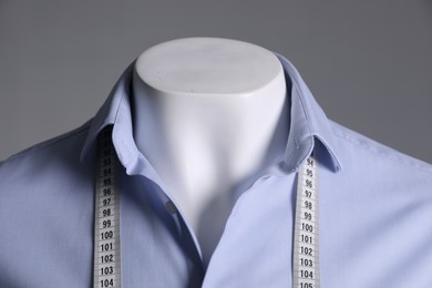 Male mannequin with light blue shirt and measuring tape on grey background, closeup