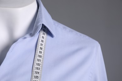 Mannequin with light blue shirt and measuring tape on grey background, closeup