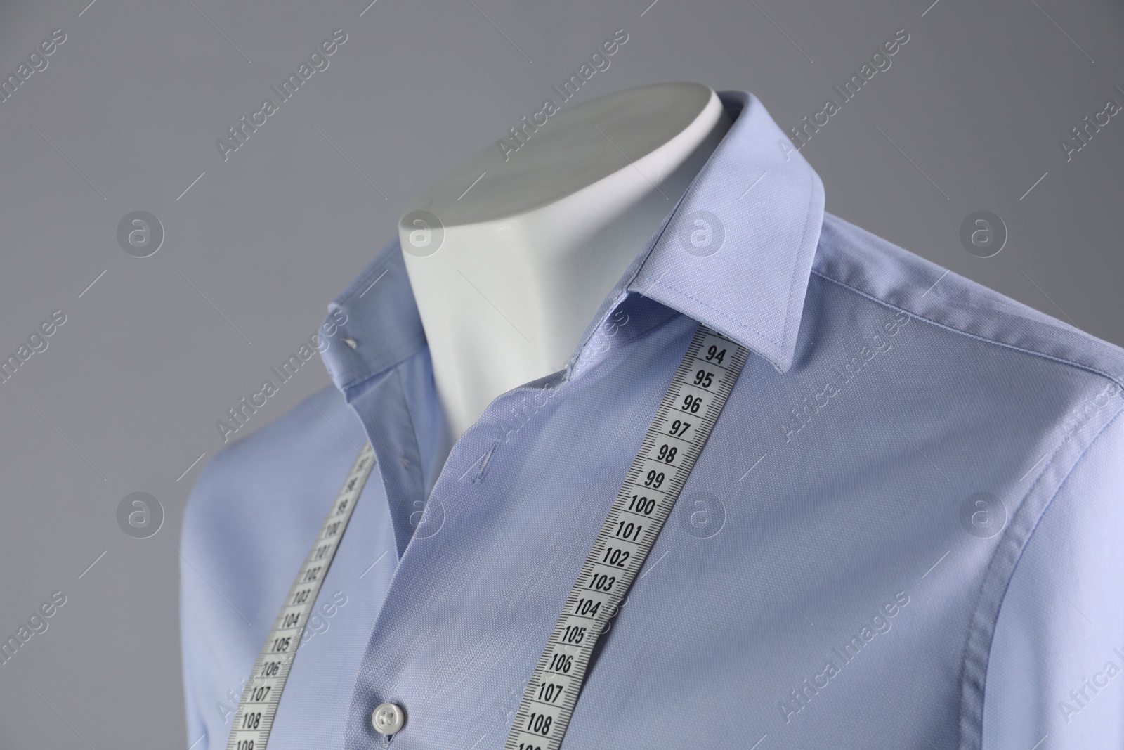 Photo of Male mannequin with light blue shirt and measuring tape on grey background, closeup