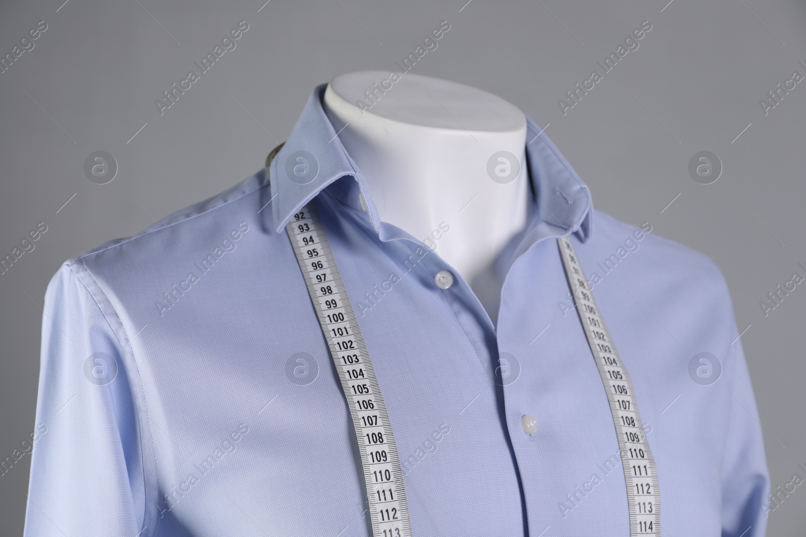 Photo of Male mannequin with light blue shirt and measuring tape on grey background, closeup