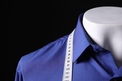 Male mannequin with blue shirt and measuring tape on black background, closeup