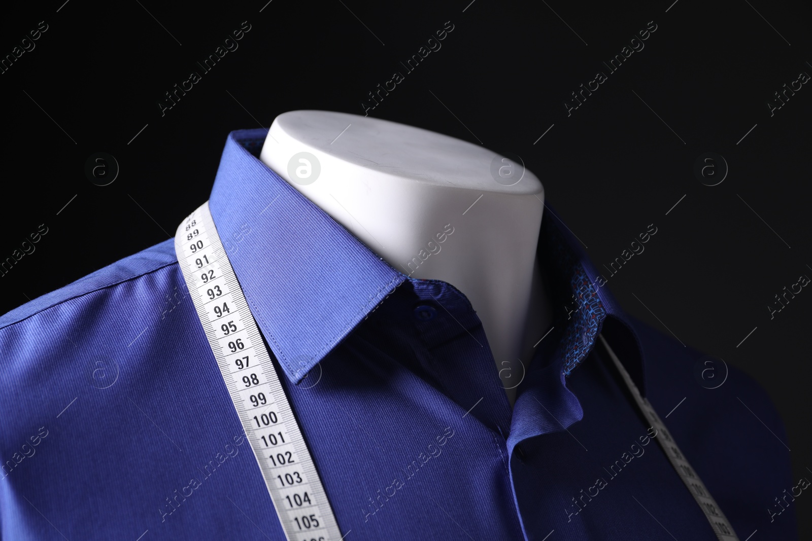 Photo of Male mannequin with blue shirt and measuring tape on black background, closeup