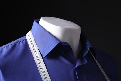 Male mannequin with blue shirt and measuring tape on black background, closeup