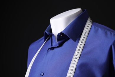 Male mannequin with blue shirt and measuring tape on black background, closeup