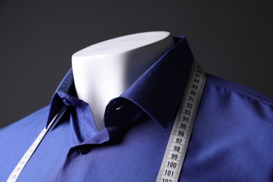 Photo of Male mannequin with blue shirt and measuring tape on black background, closeup