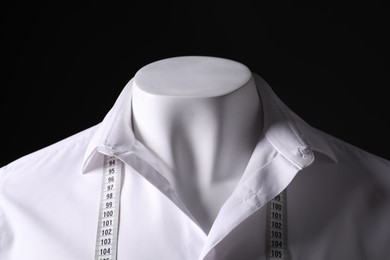 Male mannequin with white shirt and measuring tape on black background, closeup