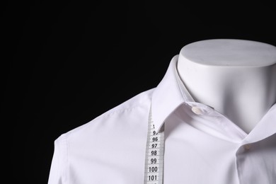 Male mannequin with white shirt and measuring tape on black background, closeup