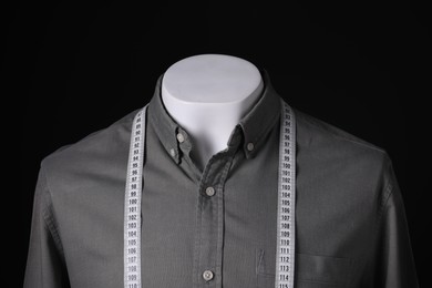 Male mannequin with grey shirt and measuring tape on black background, closeup