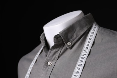 Male mannequin with grey shirt and measuring tape on black background, closeup