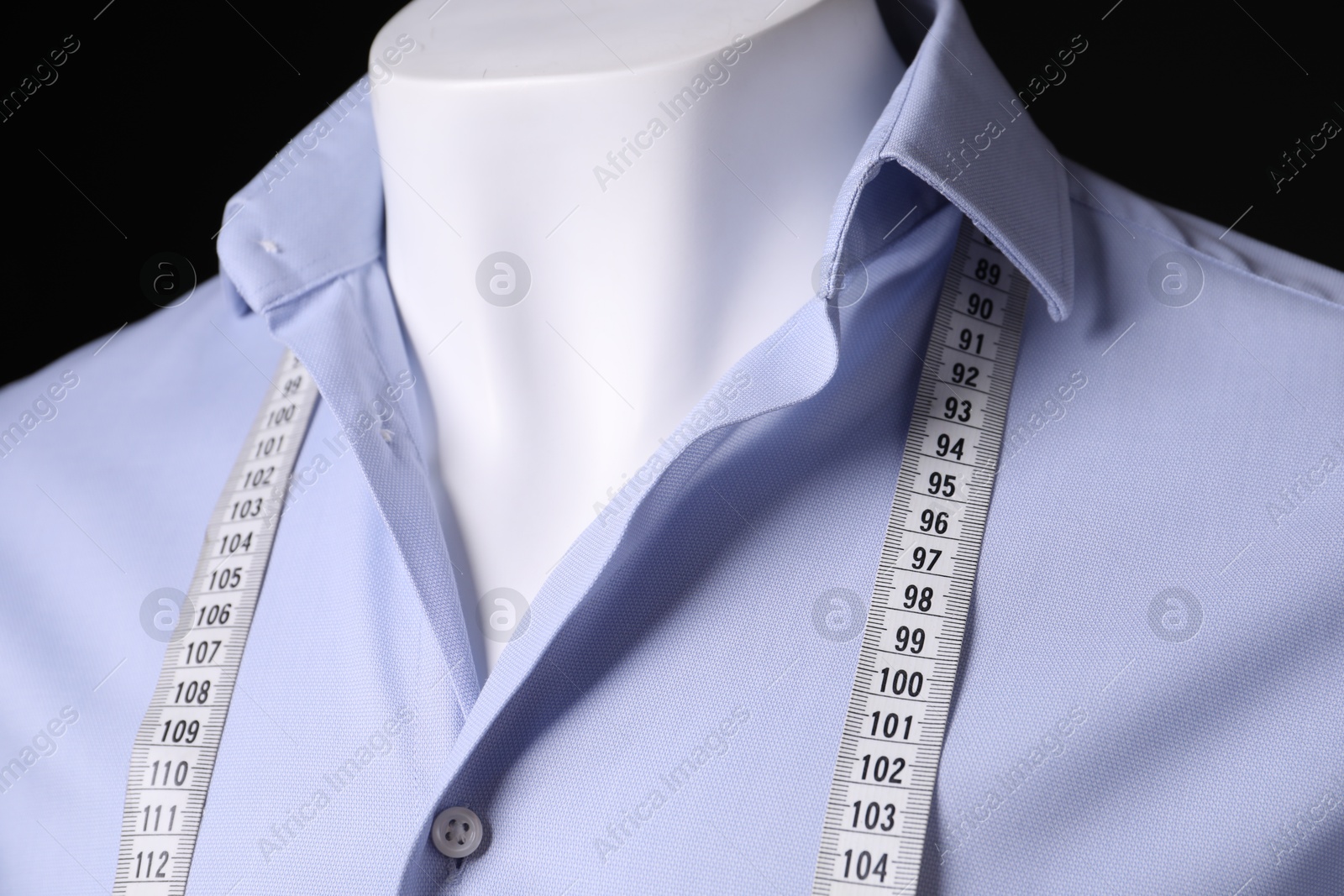 Photo of Male mannequin with light blue shirt and measuring tape on black background, closeup