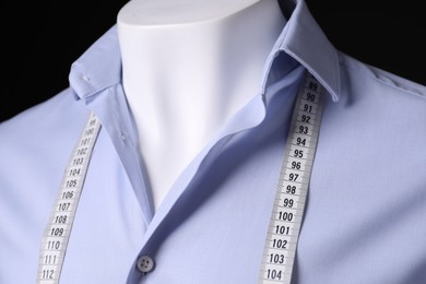 Male mannequin with light blue shirt and measuring tape on black background, closeup