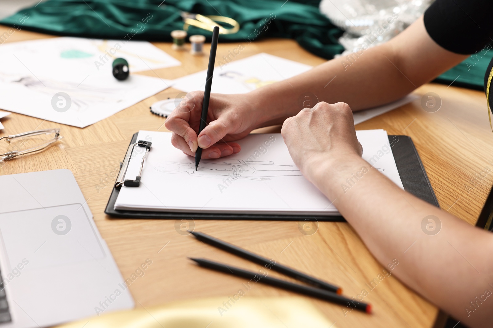 Photo of Fashion designer drawing sketch of beautiful outfit at wooden table, closeup