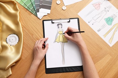 Fashion designer drawing sketch of beautiful dress at wooden table, top view