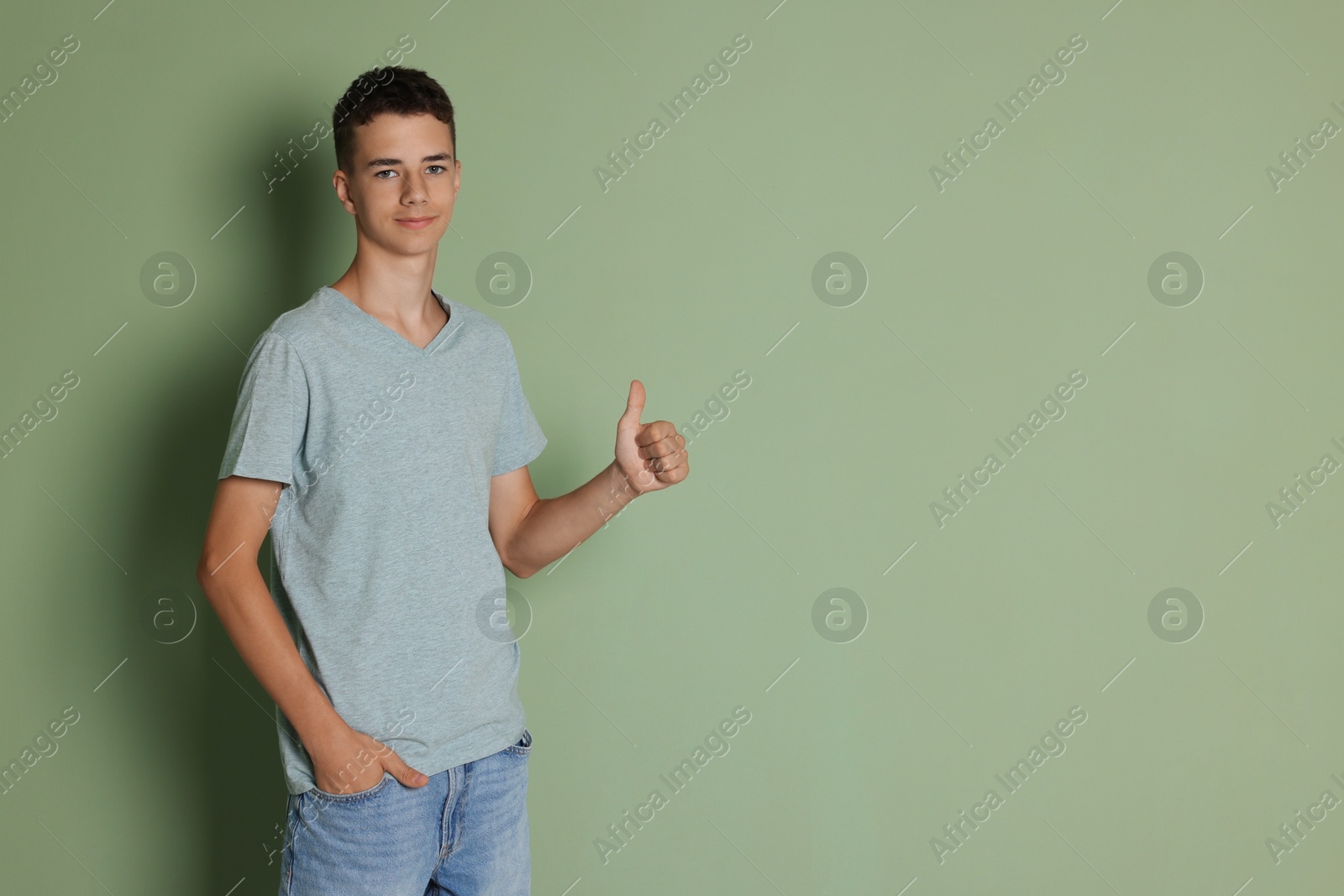 Photo of Teenage boy wearing light grey t-shirt and showing thumbs up on green background, space for text