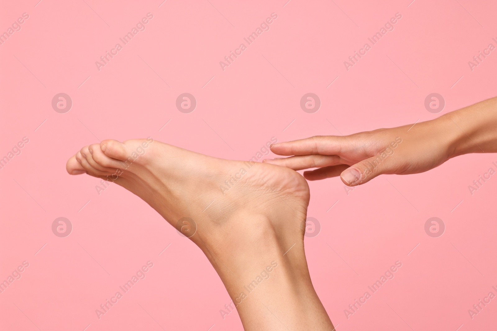 Photo of Woman touching her smooth feet on pink background, closeup