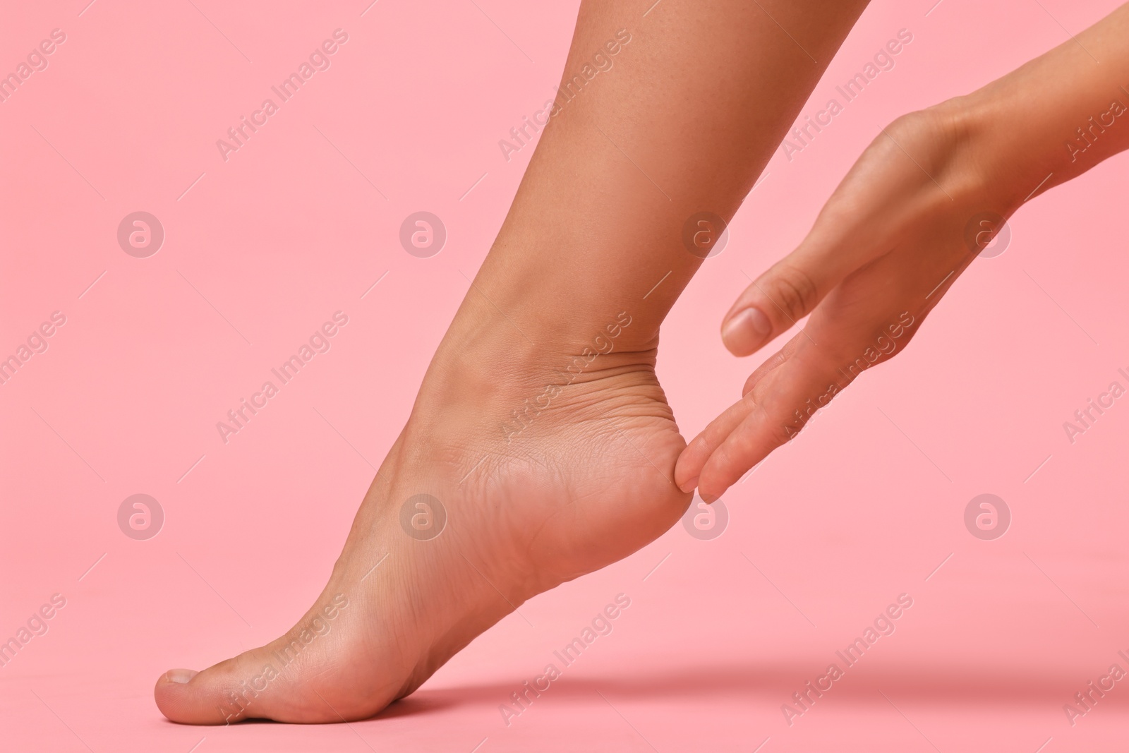 Photo of Woman touching her smooth feet on pink background, closeup