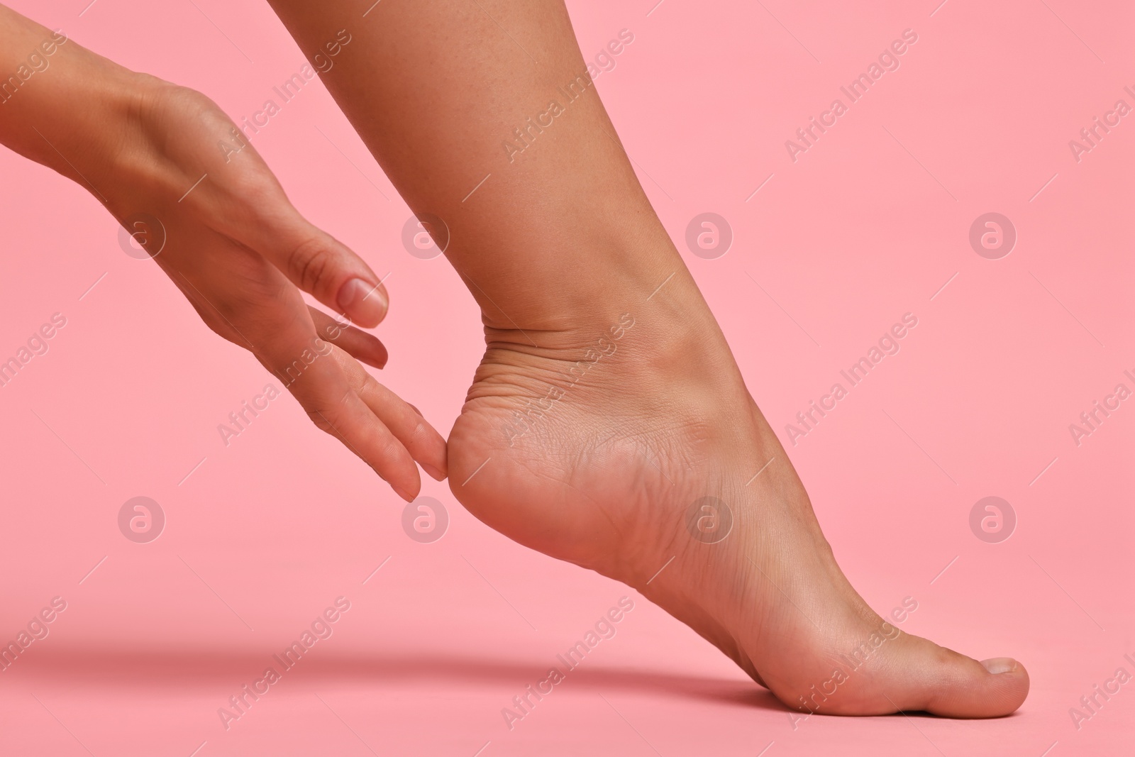 Photo of Woman touching her smooth feet on pink background, closeup