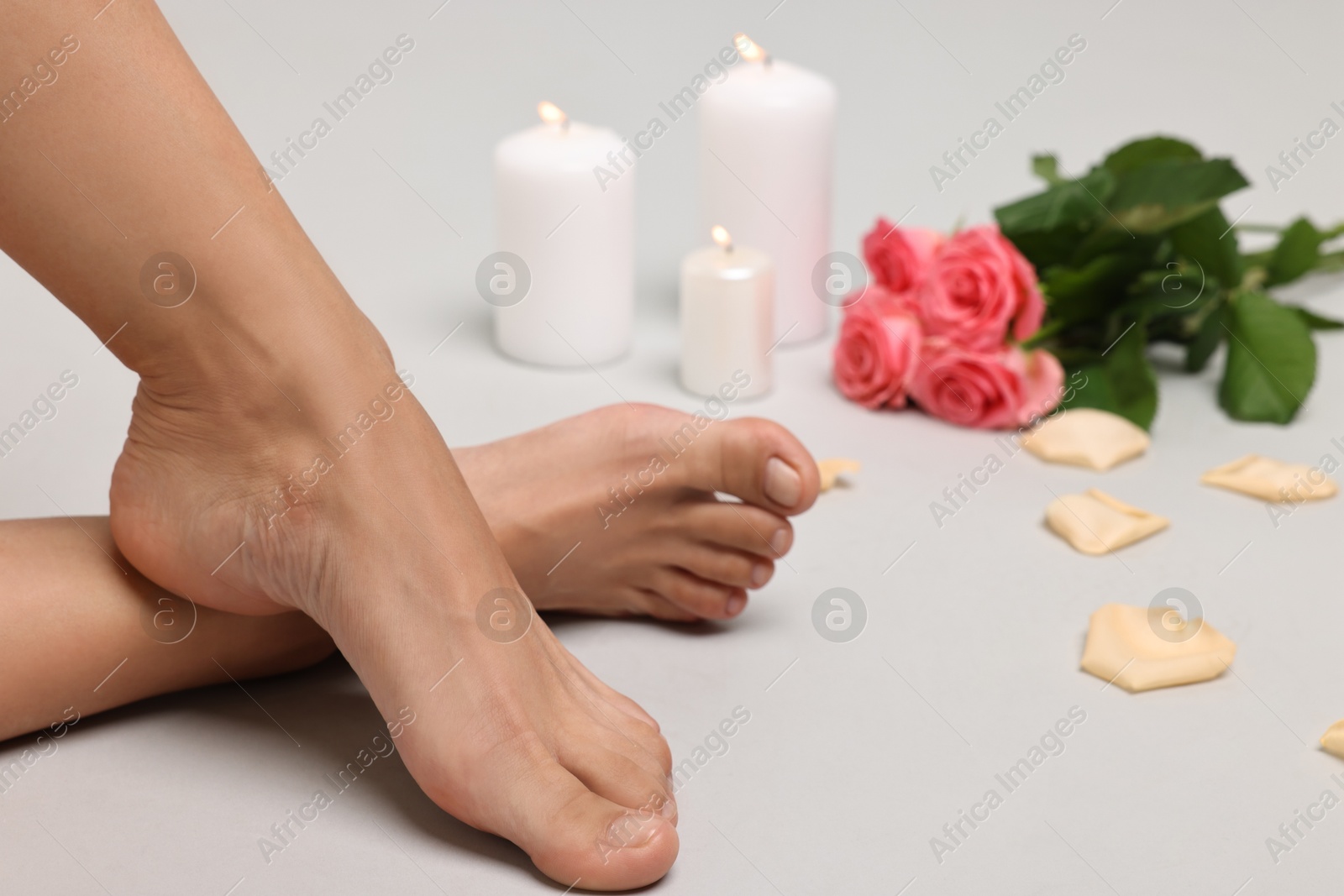 Photo of Woman with smooth feet, burning candles, petals and flowers on grey background, closeup