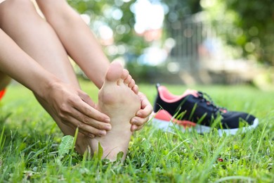 Photo of Woman suffering from foot pain on green grass outdoors, closeup