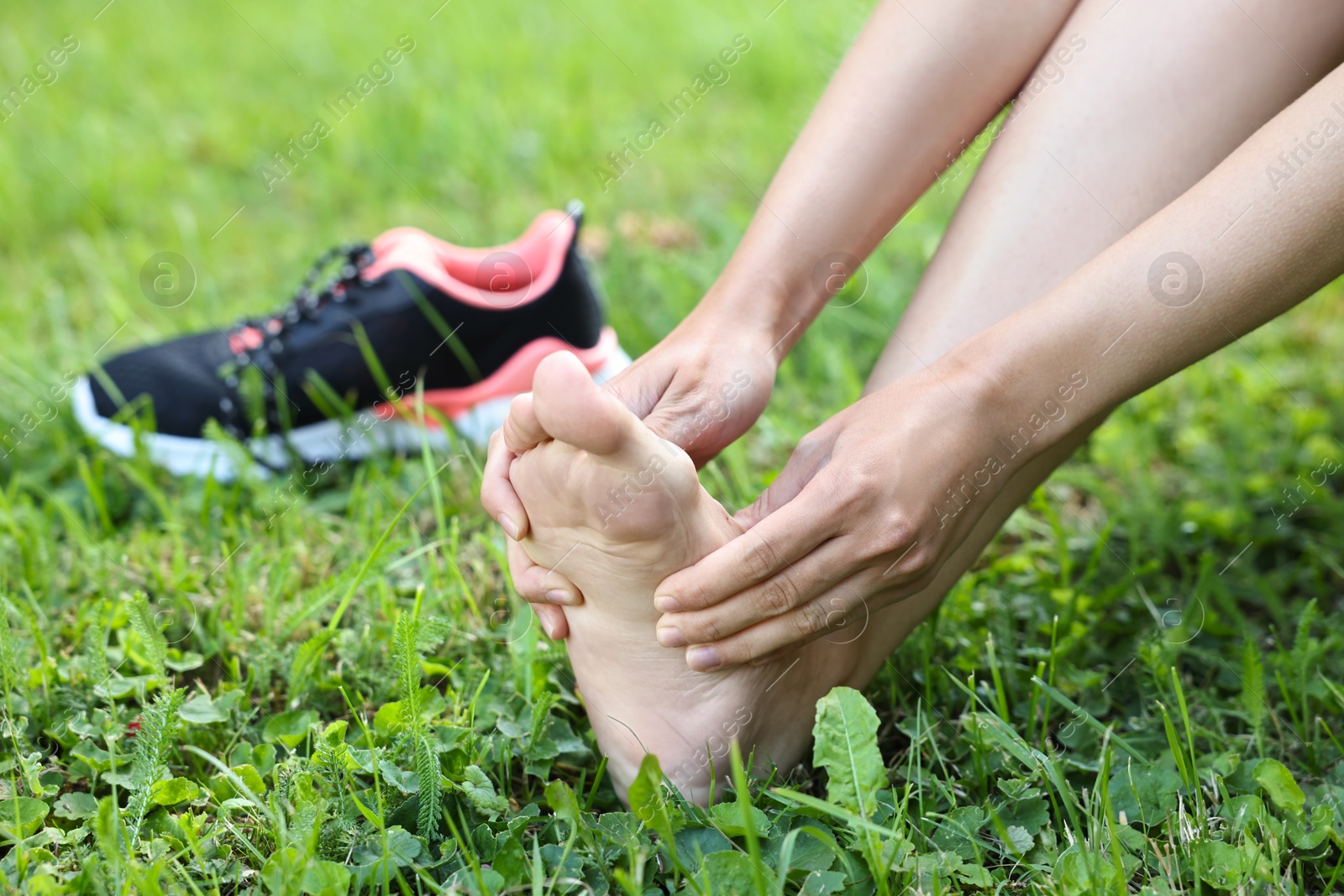 Photo of Woman suffering from foot pain on green grass outdoors, closeup