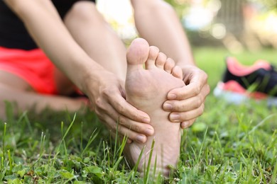 Photo of Woman suffering from foot pain on green grass outdoors, closeup