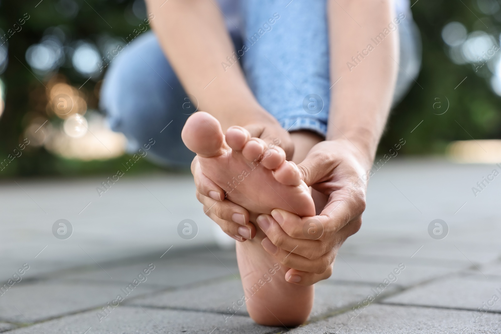 Photo of Woman suffering from foot pain outdoors, closeup