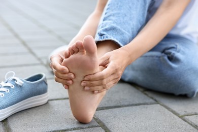 Photo of Woman suffering from foot pain outdoors, closeup