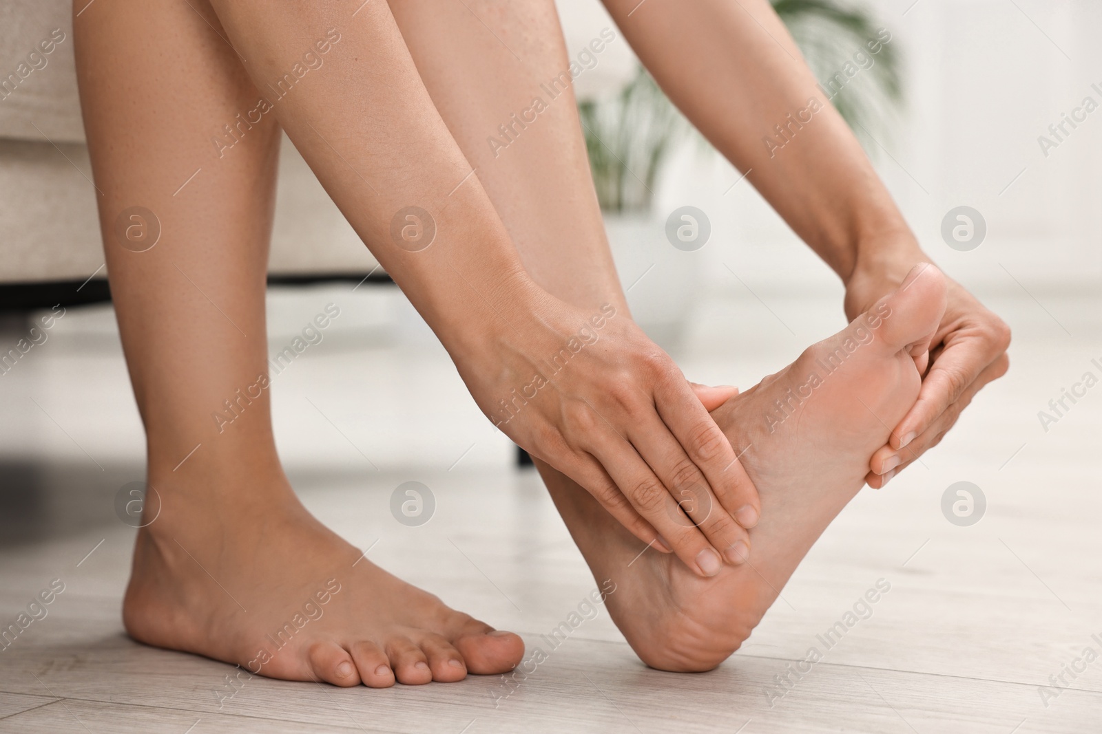 Photo of Woman suffering from foot pain at home, closeup