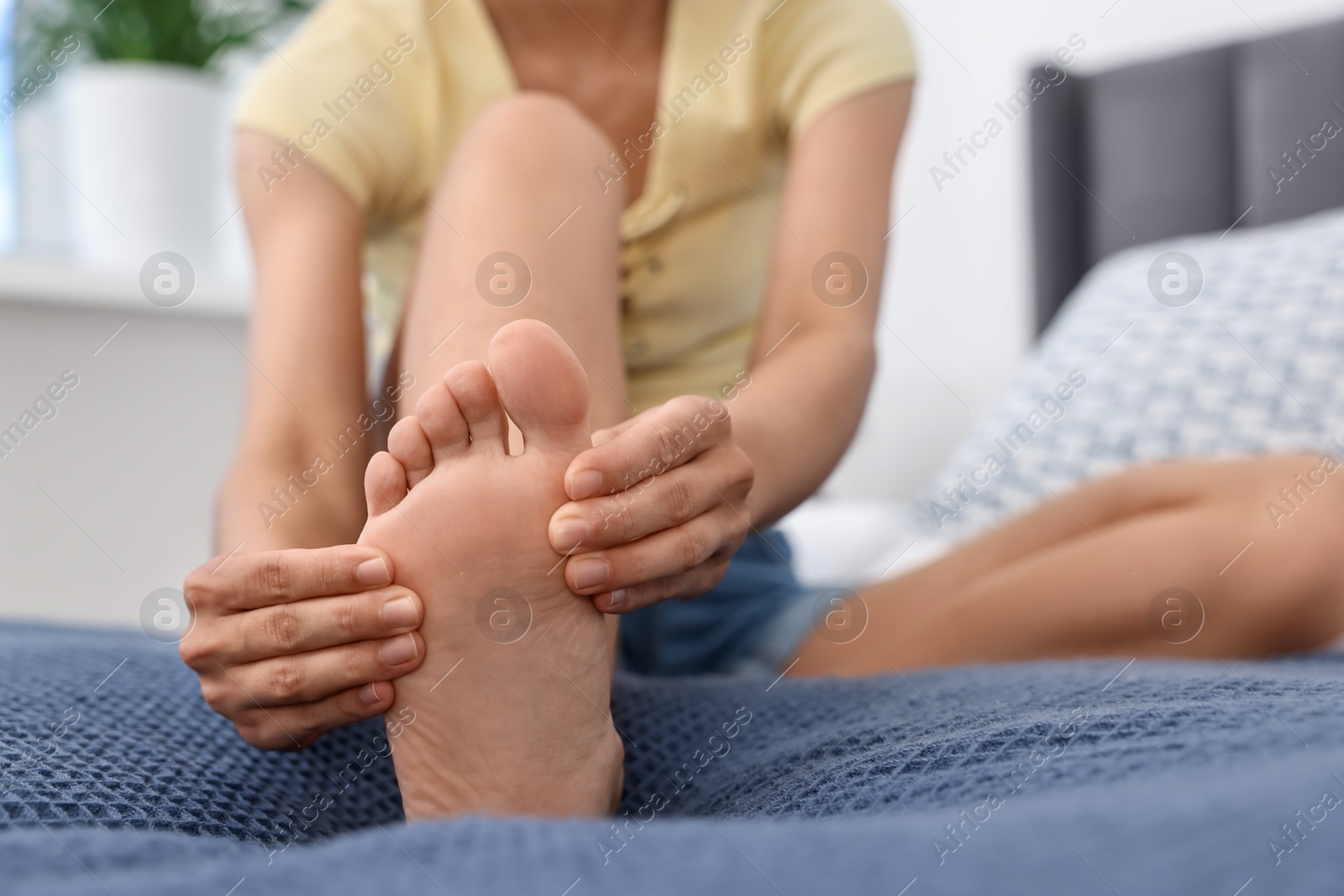 Photo of Woman suffering from foot pain on bed at home, closeup