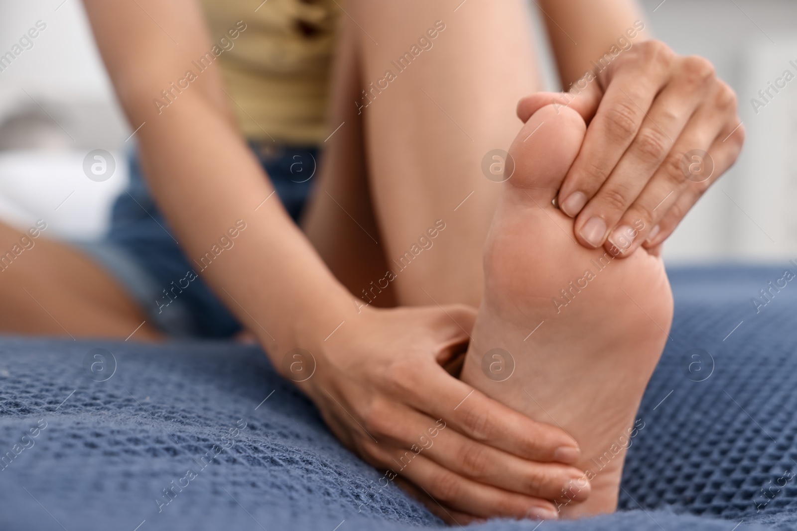 Photo of Woman suffering from foot pain on bed at home, closeup