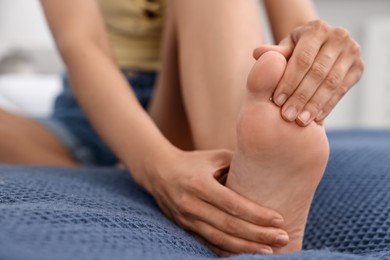 Photo of Woman suffering from foot pain on bed at home, closeup