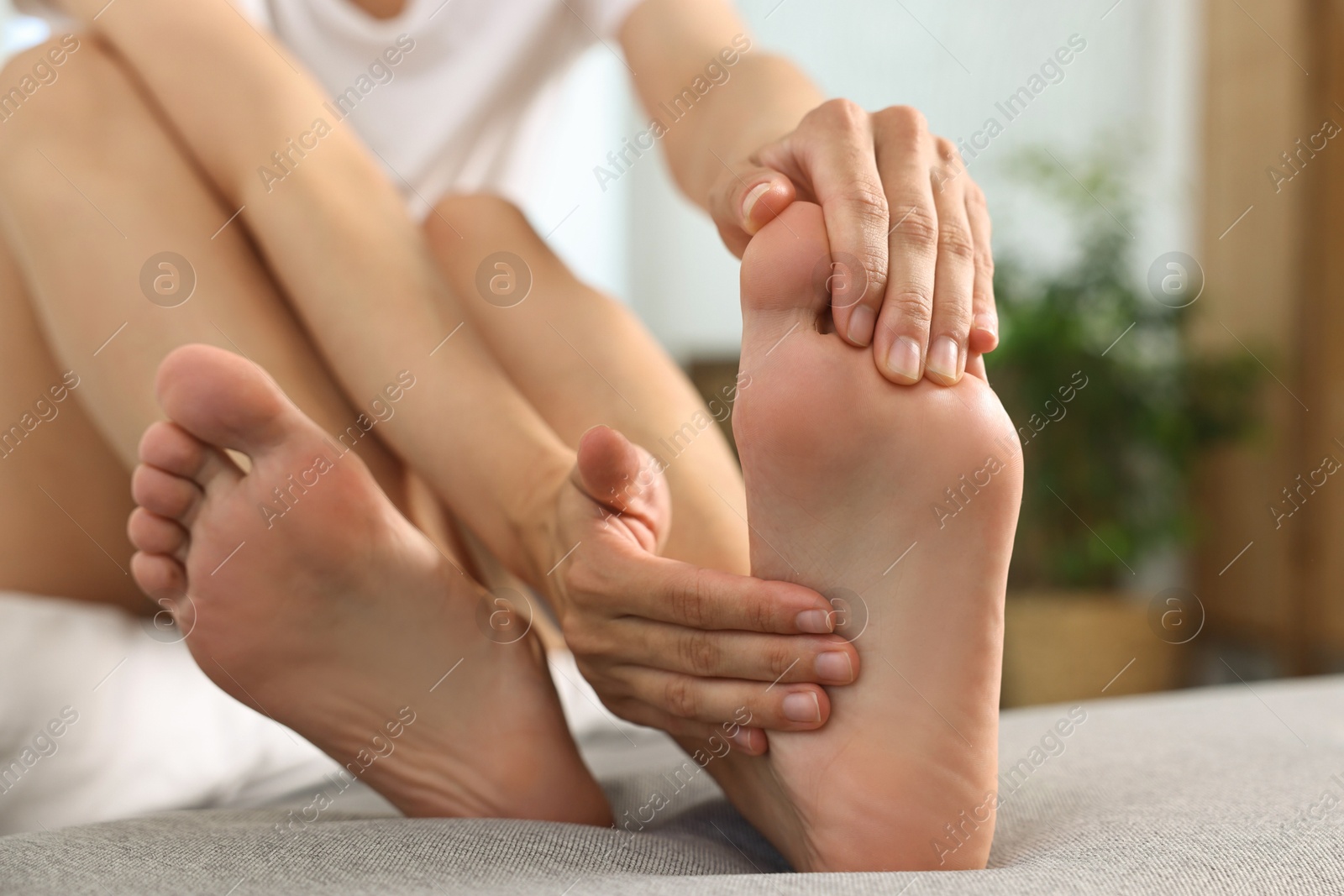 Photo of Woman suffering from foot pain on bed at home, closeup