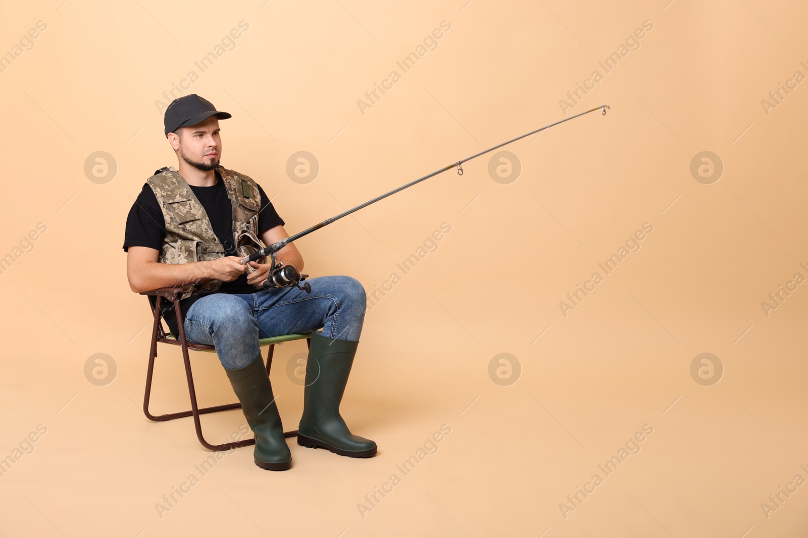 Photo of Fisherman with rod fishing on chair against beige background