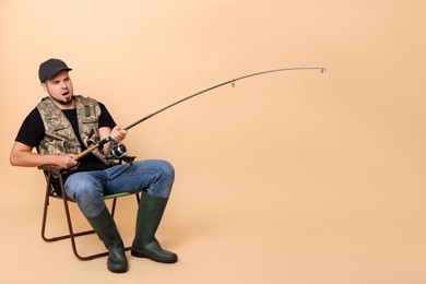 Photo of Emotional fisherman with rod fishing on chair against beige background