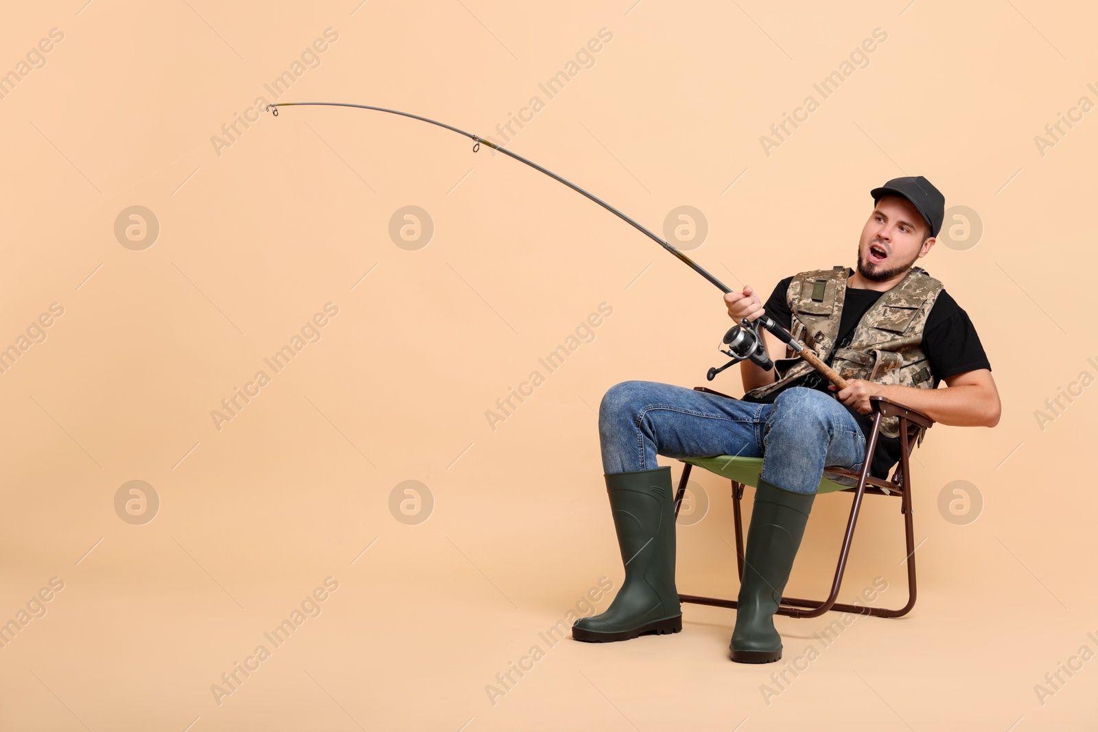 Photo of Emotional fisherman with rod fishing on chair against beige background