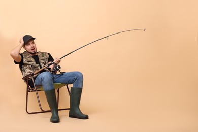 Photo of Emotional fisherman with rod fishing on chair against beige background