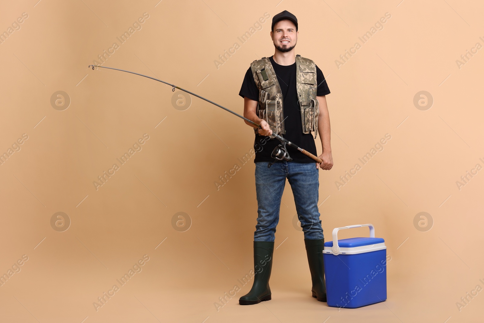 Photo of Smiling fisherman with rod and cooler box fishing on beige background